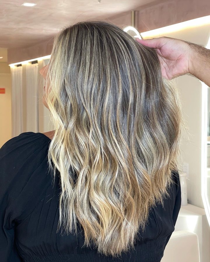 Cabelo loiro com mechas iluminadas e ondas, visto de costas
